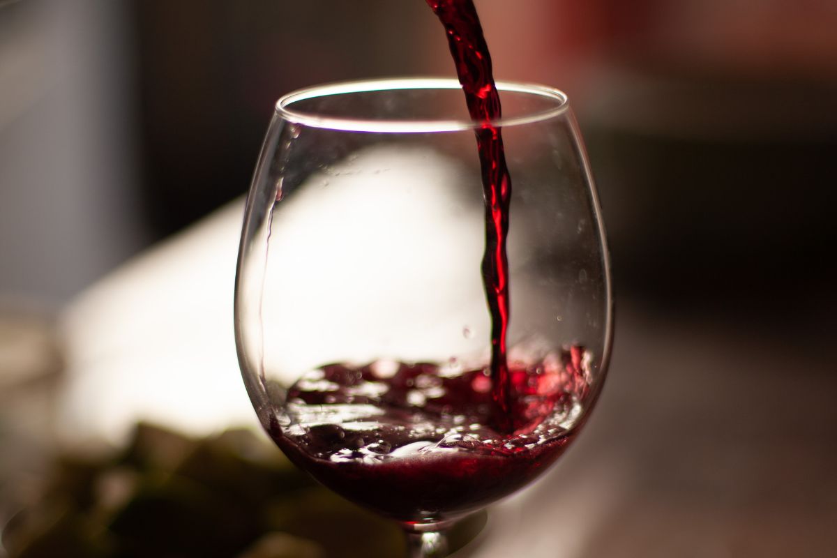 Persona sirviendo vino tinto en copa de vidrio. Foto de Canva.