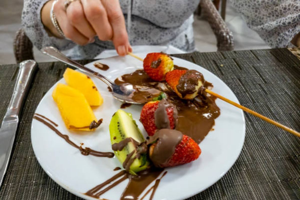 Persona comiendo fruta fresca con chocolate oscuro. Foto de Pexels.
