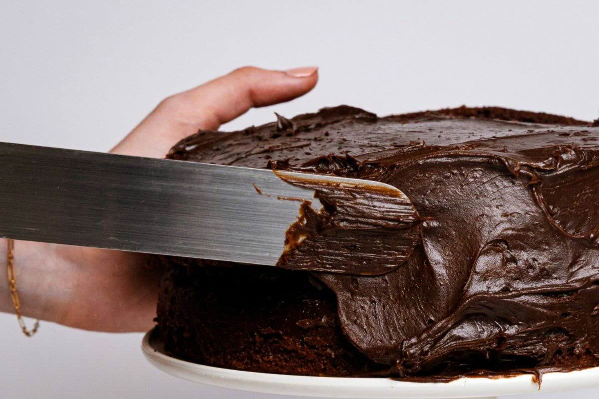 Persona cubriendo paste con betún de chocolate. Foto de Canva.