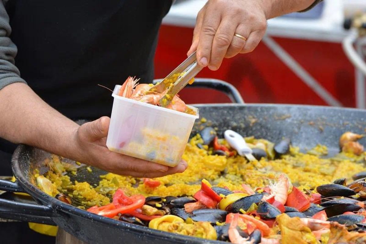 Persona agregando camarones completos a paella. Foto de Rawpixel.