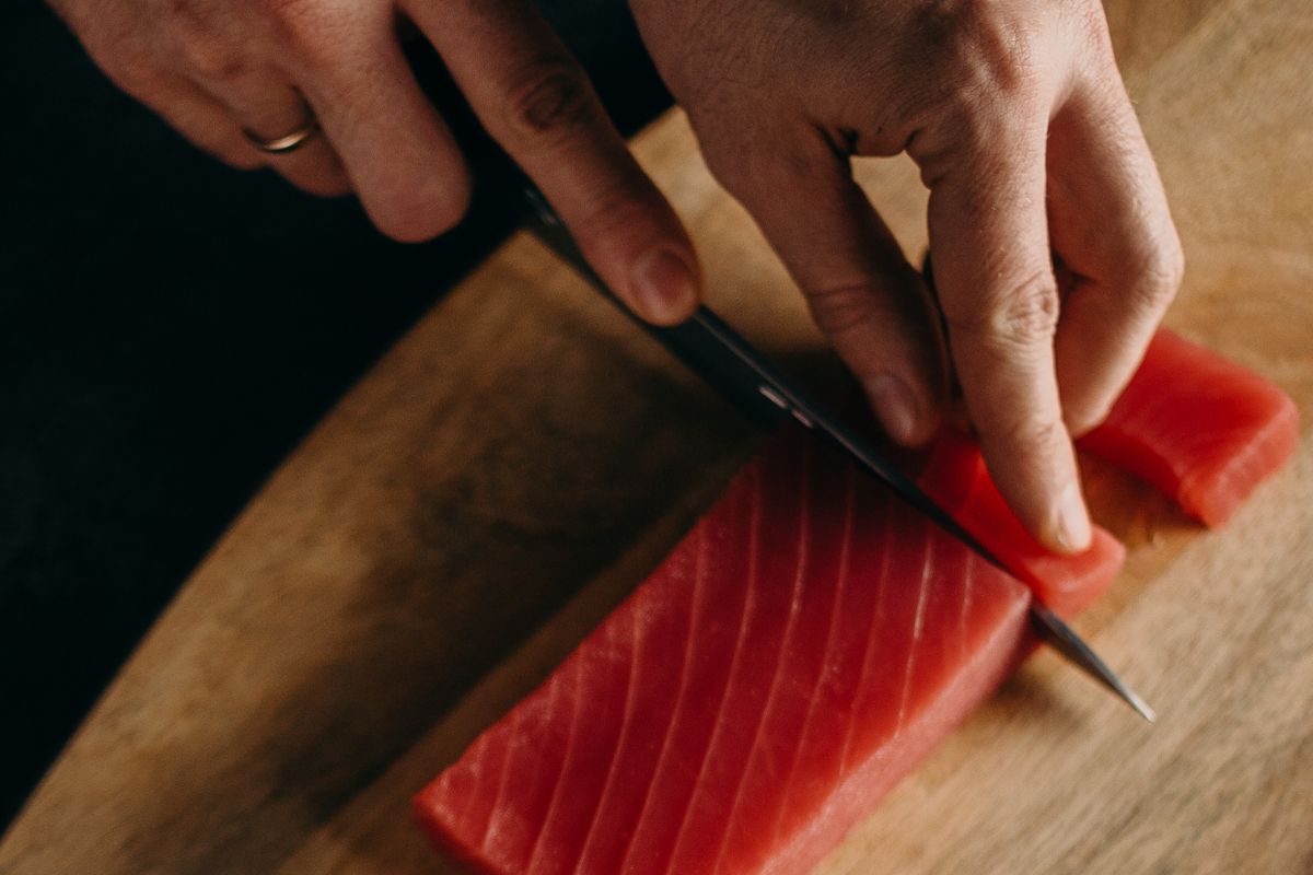Persona cortando porciones de atún fresco. Foto de Canva.