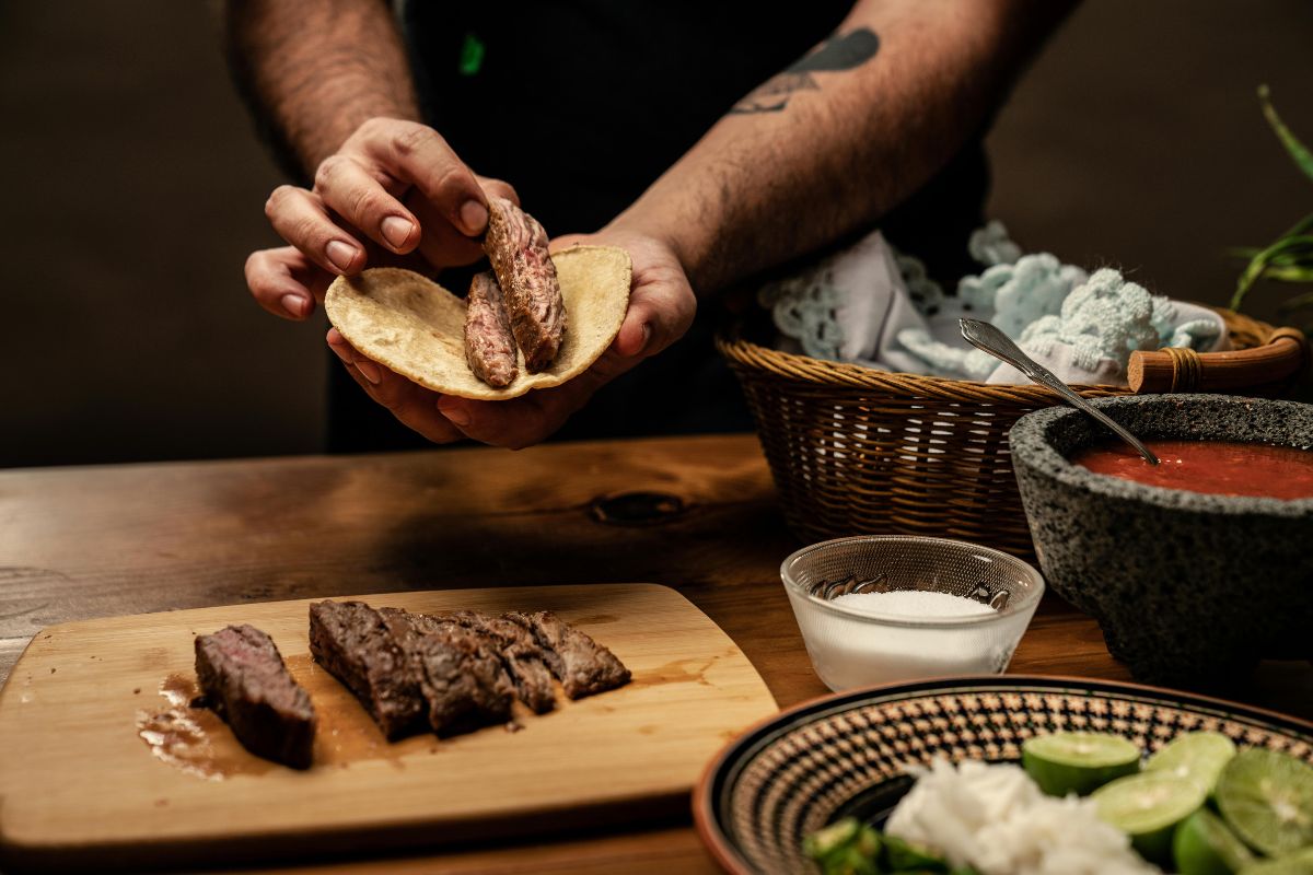 Persona preparando tacos con carne de res asada. Foto de Pexels.