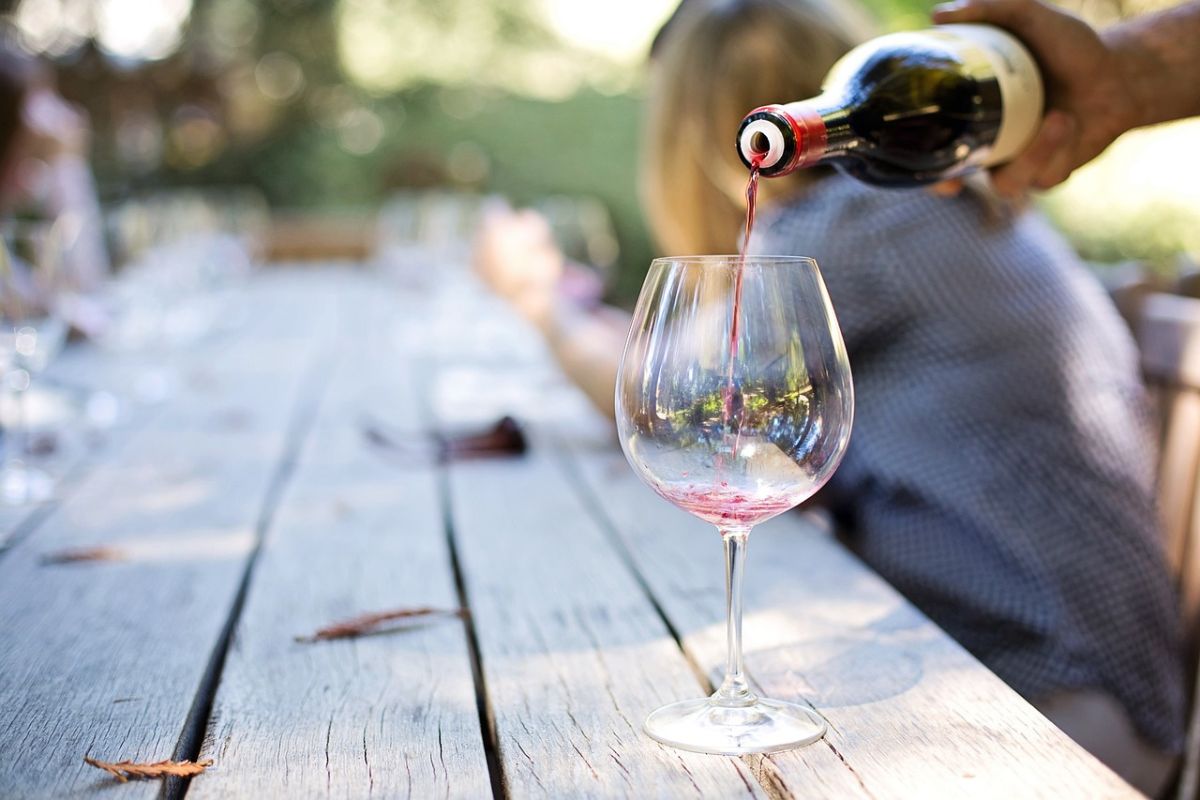 Persona sirviendo vino tinto en copa de cristal. Foto de Pixabay.com