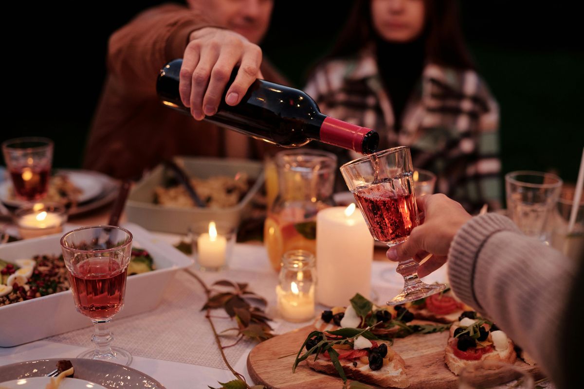 Persona sirviendo vino rosado en copa de cristal. Foto de Pexels.