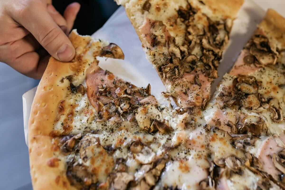 Persona tomando rebanada de pizza. Foto de Pexels.