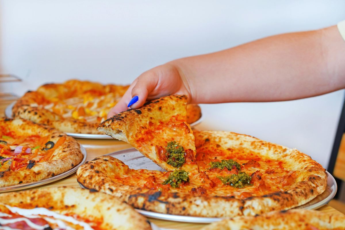 Persona tomando rebanada de pizza. Foto de Pexels.