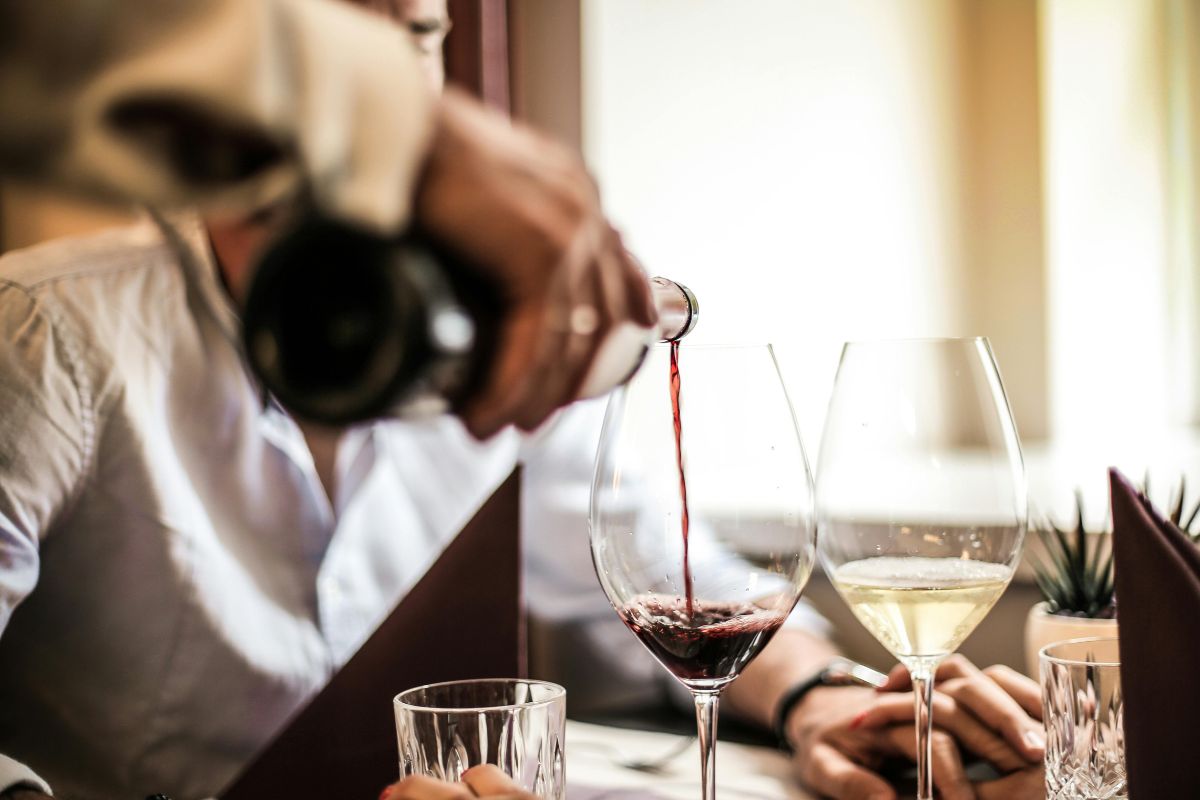 Persona sirviendo vino tinto en copa de cristal. Foto de Pexels.