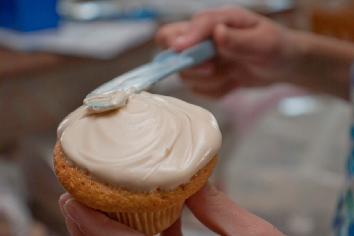 Persona cubriendo cupcakes con crema. Foto de Pexels.