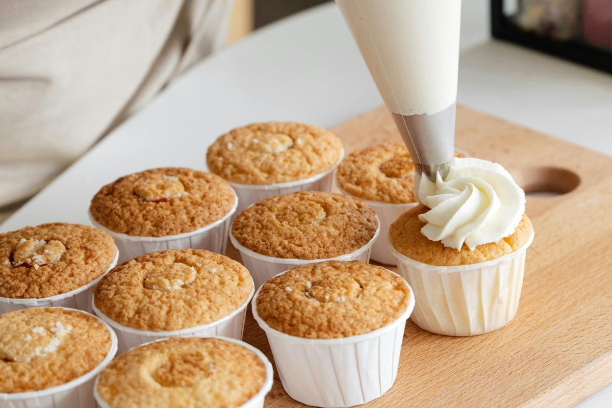 Persona decorando cupcakes con crema de mantequilla. Foto de Pexels.