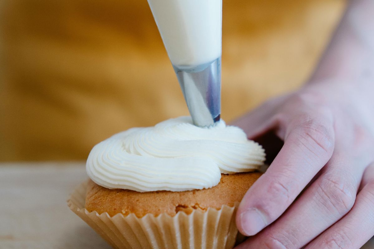 Persona decorando cupcakes con crema de mantequilla. Foto de Pexels.