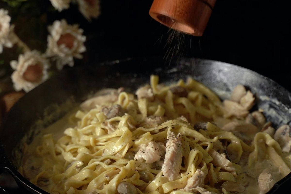 Persona añadiendo pimienta molida a plato de pasta. Foto de Pexels.