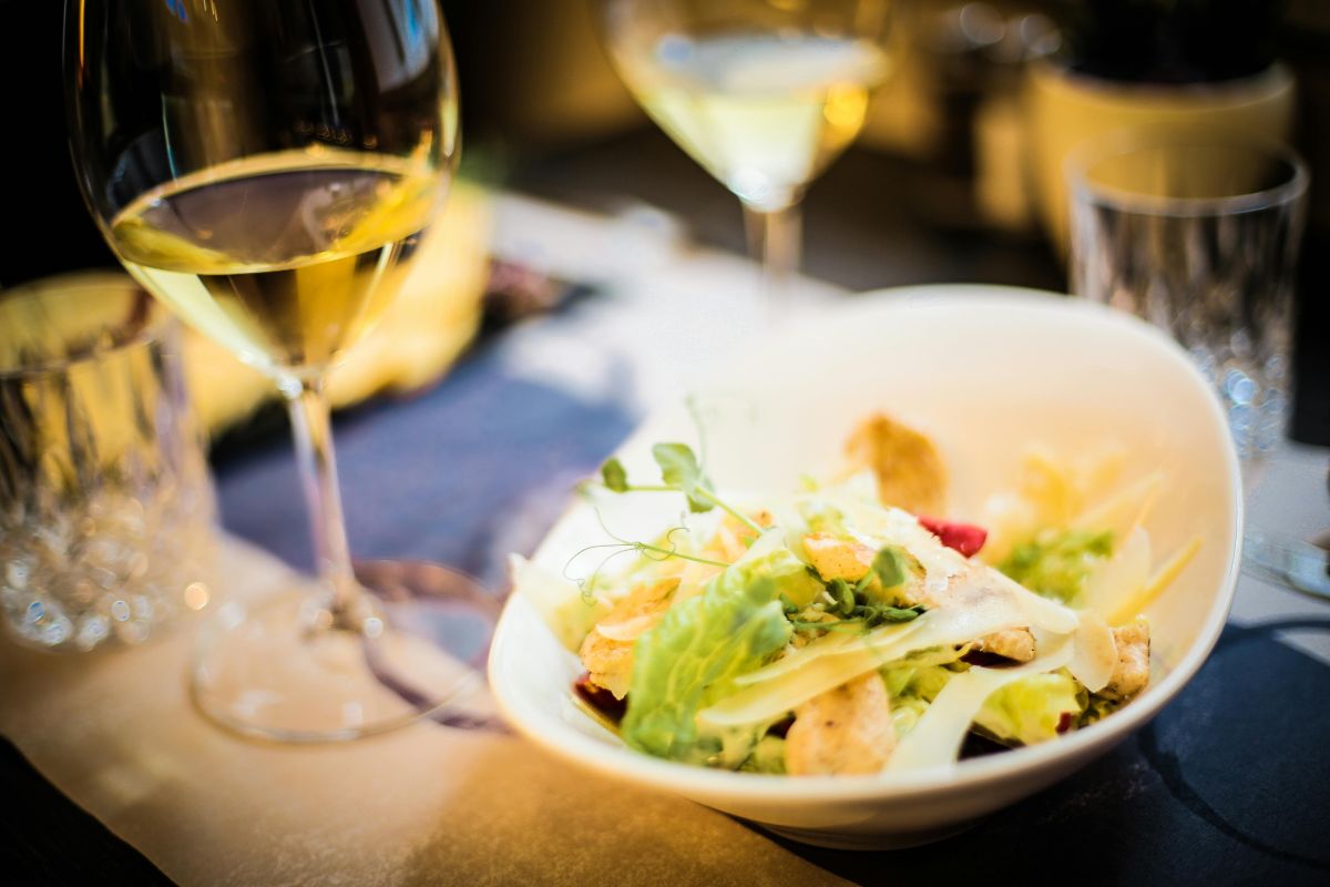 Cena acompañada de vino blanco. Foto de Pexels.