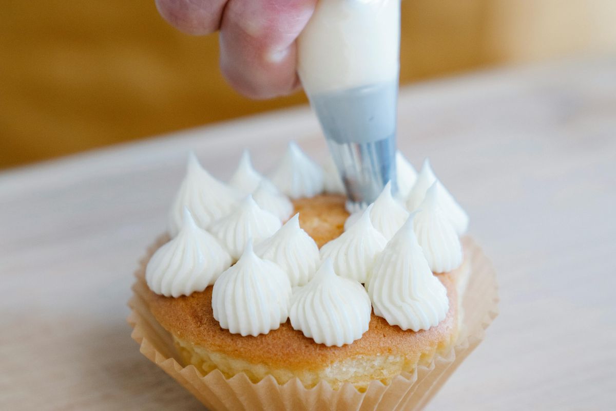 Persona decorando cupcake con crema dulce. Foto de Pexels.