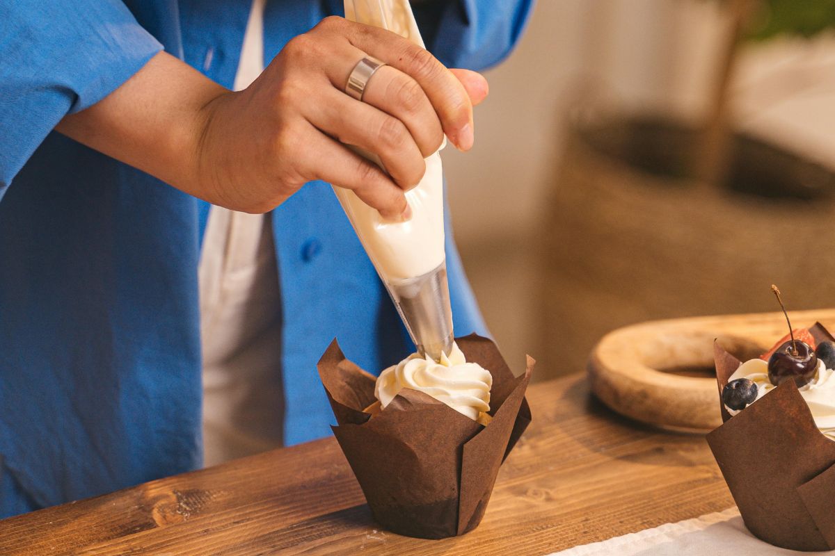 Persona decorando cupcake con crema dulce. Foto de Pexels.