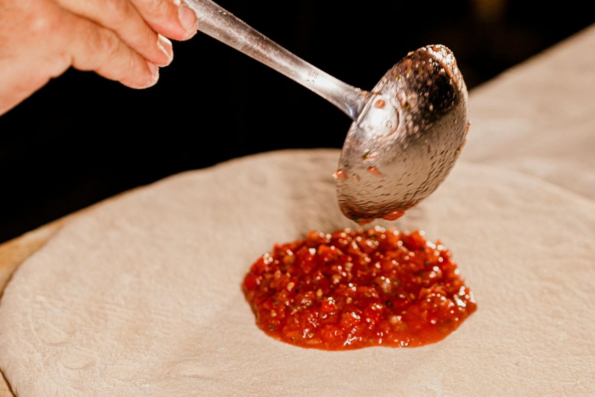 Salsa de tomate sobre masa para pizza. Foto de Pexels.